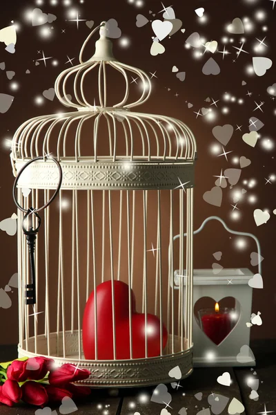 Heart in decorative cage on wooden table, on brown background — Stock Photo, Image