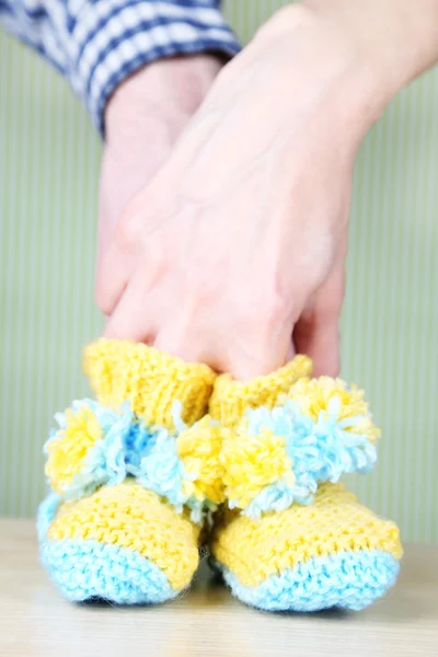 Hands with crocheted booties for baby, on color background — Stock Photo, Image