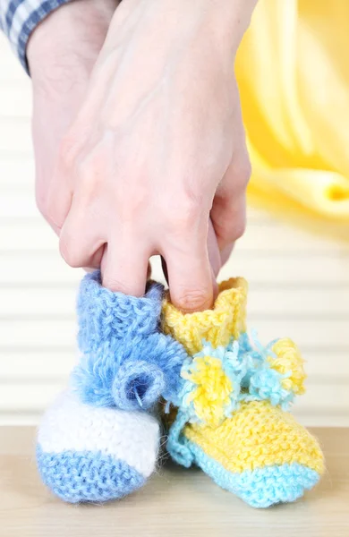 Hands with crocheted booties for baby, on light background — Stock Photo, Image