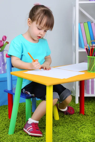 Маленькая девочка рисует сидя за столом в комнате — стоковое фото