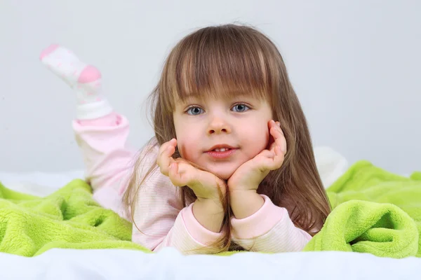 Kleines Mädchen liegt auf Bett auf Wandhintergrund — Stockfoto