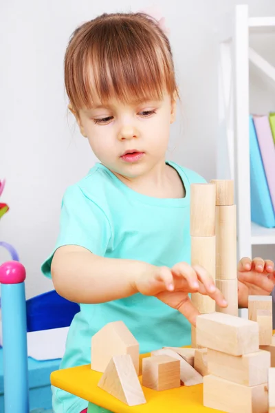 Little girl plays with construction blocks sitting at table in room — Stock Photo, Image