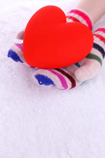 Mãos femininas em mitenes com coração no fundo da neve — Fotografia de Stock