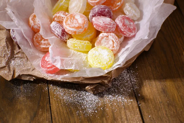 Sweet multicolor candies on paper, on wooden background — Stock Photo, Image