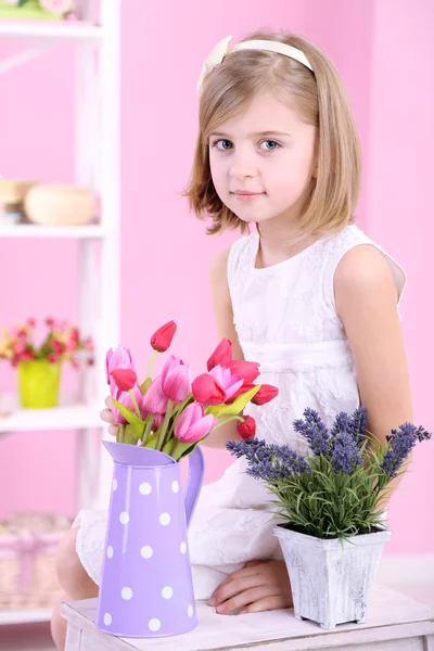 Liten flicka sitter på liten stege med blommor på rosa bakgrund — Stockfoto