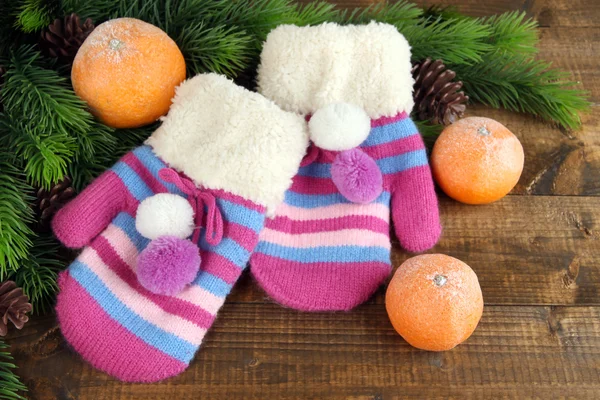 Striped mittens with fir branches and tangerines on wooden background — Stock Photo, Image