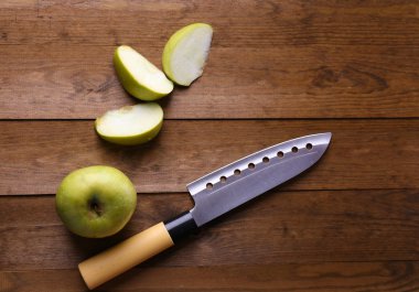 Mutfak bıçağı ve yeşil elma, ahşap arka planda.