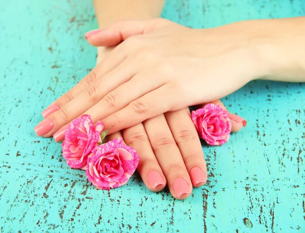 Mani donna con manicure rosa e fiori, su sfondo colore — Foto Stock