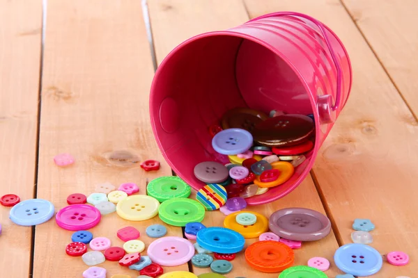 Colorful buttons strewn from bucket on wooden background — Stock Photo, Image