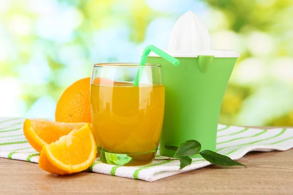 Imprensa de citrinos, copo de suco e laranjas maduras na mesa de madeira marrom — Fotografia de Stock