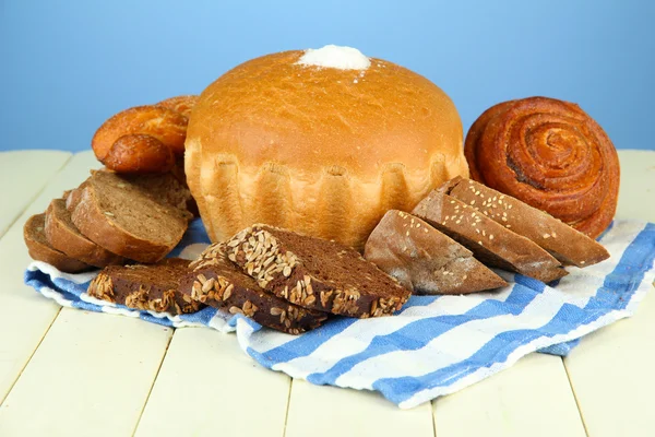Composition with bread, rolls and napkin on wooden table, on color background — Stock Photo, Image
