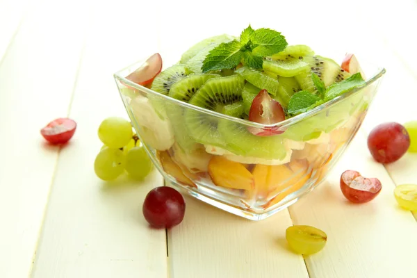 Smakelijke fruitsalade in glazen kom, op witte houten tafel — Stockfoto