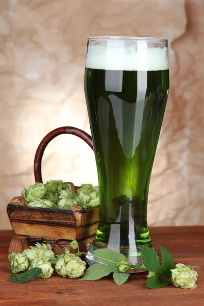 Glass of green beer and hops, on wooden table — Stock Photo, Image