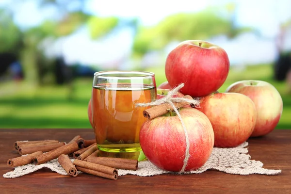 Manzanas maduras con palitos de canela y vaso de bebida de manzana sobre mesa de madera, sobre fondo brillante —  Fotos de Stock