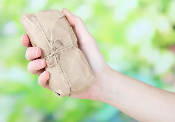 Woman hand holding a telephone wrapped in brown kraft paper, on nature background — Stock Photo, Image