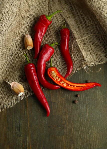 Chiles rojos picantes y ajo, sobre tela de saco, sobre fondo de madera — Foto de Stock