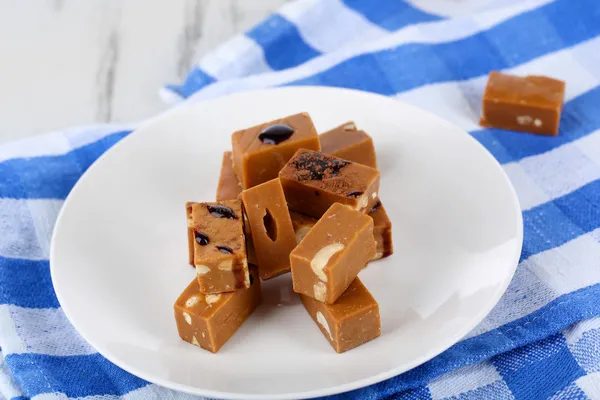 Many toffee on plate on napkin on wooden table — Stock Photo, Image