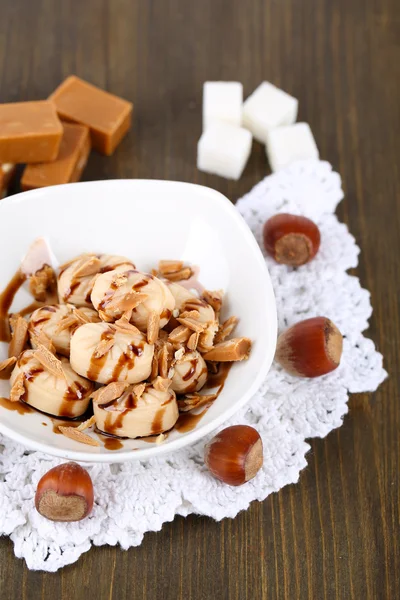 Many toffee in bowl on napkin on wooden table — Stock Photo, Image