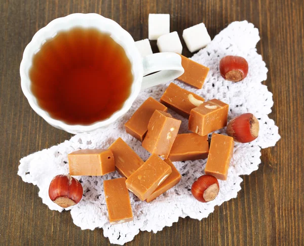 Banyak toffee dan cangkir teh di serbet di atas meja kayu — Stok Foto