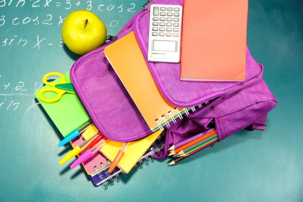 Zaino viola con materiale scolastico su sfondo verde scrivania — Foto Stock