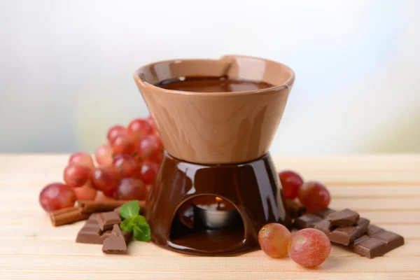 Schokoladenfondue mit Früchten, auf Holztisch, auf hellem Hintergrund — Stockfoto