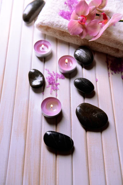 Still life with beautiful blooming orchid flower, towel and spa stones, on color wooden background — Stock Photo, Image