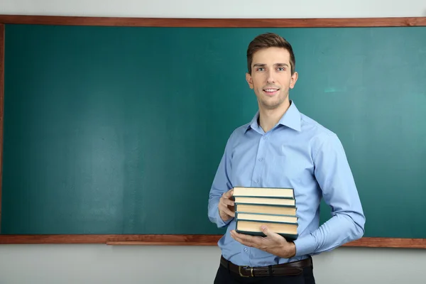 Young teacher with books near chalkboard in school classroom — Stock Photo, Image