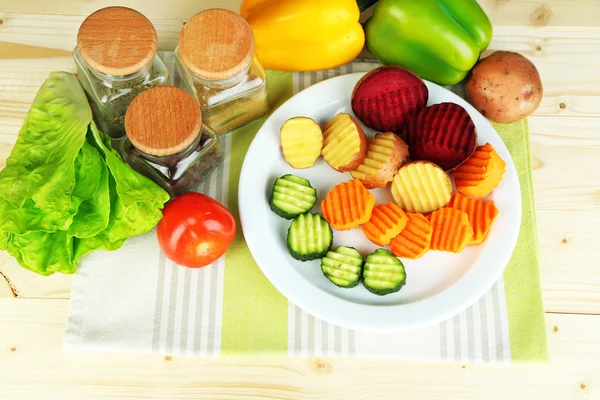 Beaux légumes tranchés, sur assiette, sur fond de bois — Photo