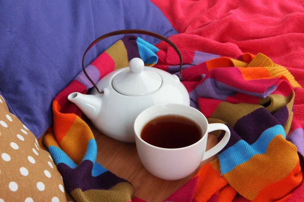 Tasse und Teekanne auf Holzständer und Schal auf dem Bett aus nächster Nähe — Stockfoto