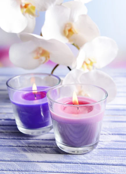 Hermosas velas de colores y flores de orquídea, sobre mesa de madera de color, sobre fondo claro —  Fotos de Stock
