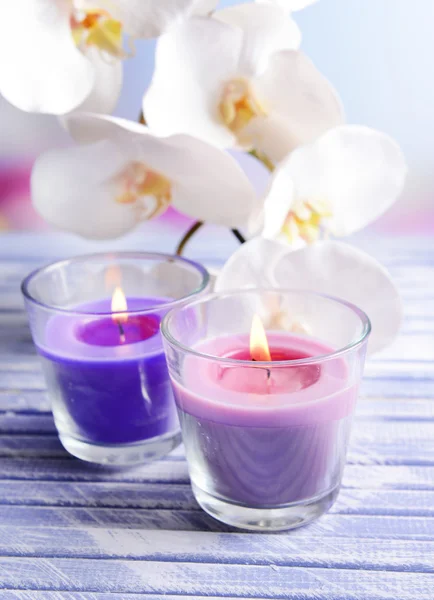 Lindas velas coloridas e flores de orquídeas, na mesa de madeira colorida, no fundo claro — Fotografia de Stock