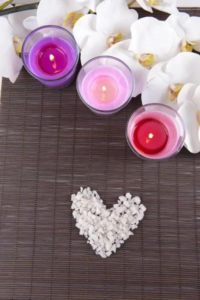 Komposition mit schönen bunten Kerzen, Meersalz und Orchideenblumen, auf Bambusmatte Hintergrund — Stockfoto