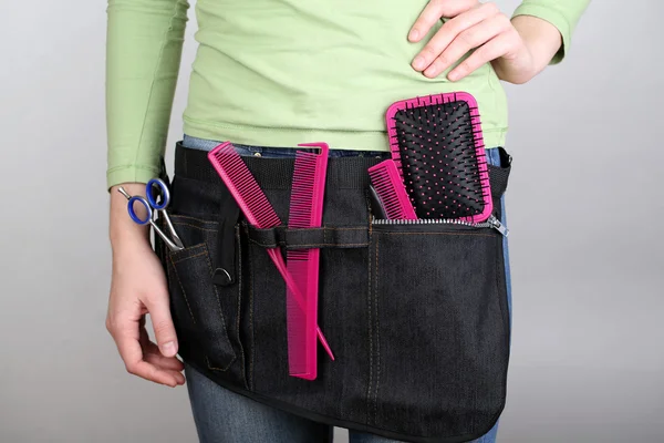 Woman hairdresser with tool belt on grey background — Stock Photo, Image