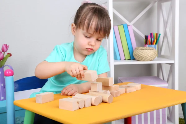 Niña juega con bloques de construcción sentada a la mesa en la habitación —  Fotos de Stock