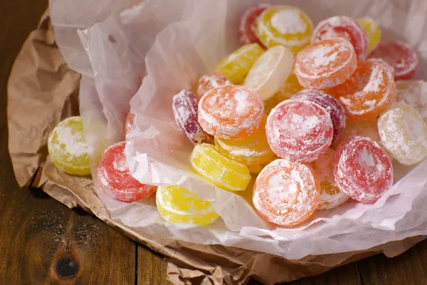 Sweet multicolor candies on paper, on wooden background — Stock Photo, Image