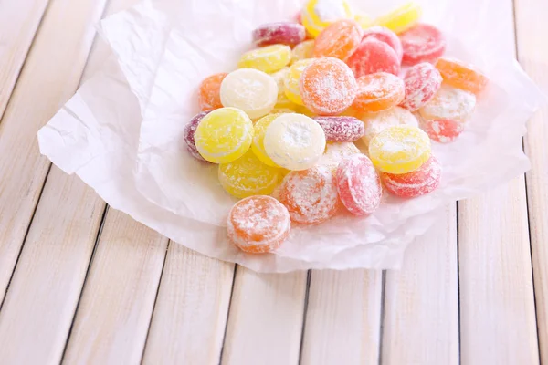 Bonbons multicolores sucrés sur papier, sur fond de bois couleur — Photo