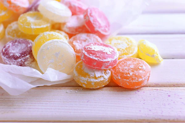 Sweet multicolor candies on paper, on color wooden background — Stock Photo, Image