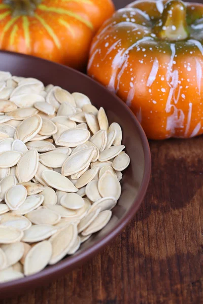 Pompoenpitten in kom met pumpkins op tafel close-up — Stockfoto