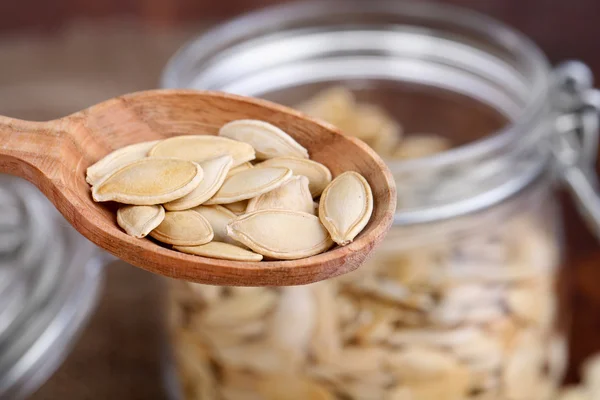 Pumpkin seeds in spoon and jar on table close up — Stock Photo, Image