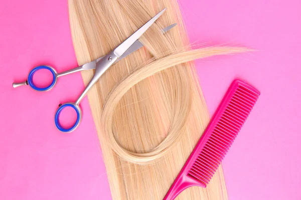 Long blond hair with comb and scissors on pink background — Stock Photo, Image