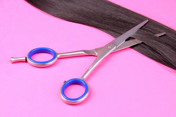 Long black hair with scissors on pink background — Stock Photo, Image