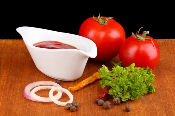 Ketchup en rijpe tomaten op houten tafel op zwarte achtergrond — Stockfoto