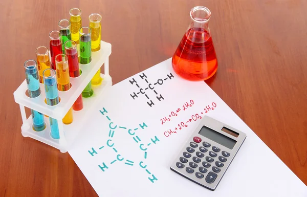 Tubos de ensayo con líquidos coloridos y fórmulas en la mesa — Foto de Stock