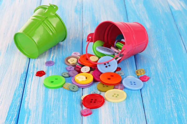 Colorful buttons strewn from buckets on wooden background — Stock Photo, Image