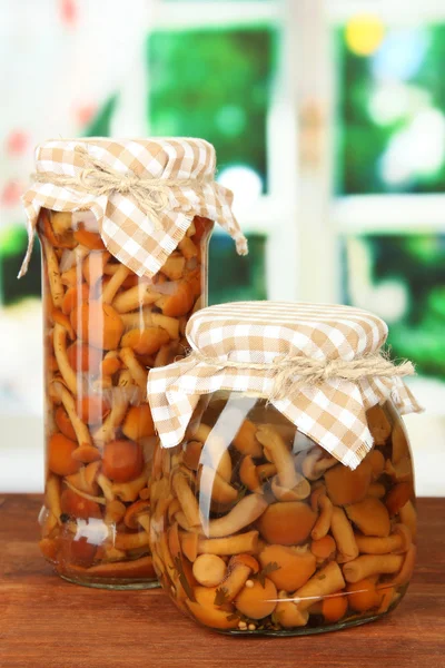 Delicious marinated mushrooms in glass jars, on wooden table on bright background — Stock Photo, Image