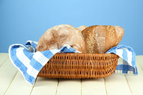 Bread in wicker basket, on wooden table, on color background — Stock Photo, Image