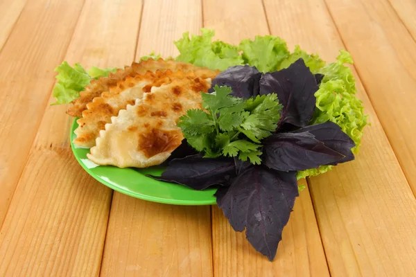 Sabrosos chebureks con hierbas frescas en el plato, sobre fondo de madera — Foto de Stock