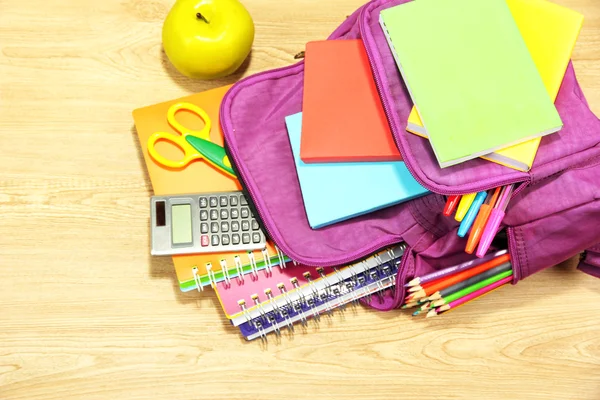 Purple backpack with school supplies on wooden background — Stock Photo, Image