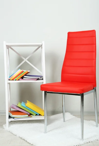 Hermoso interior con silla de color moderno, libros sobre soporte de madera, sobre fondo de pared —  Fotos de Stock