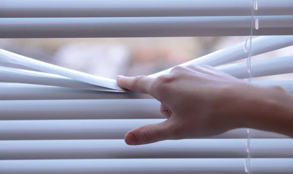 Female hand separating slats of venetian blinds with a finger to see through — Stock Photo, Image